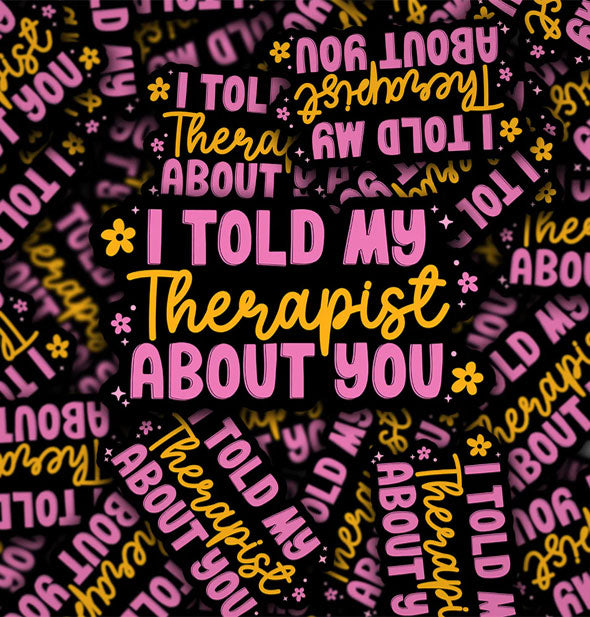 Pile of black stickers that say, "I told my therapist about you" in pink and orange lettering of alternating font styles accented by small pink and orange flowers