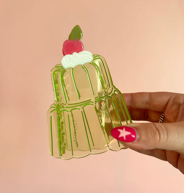 Model's hand holds a transparent green hair clip with red cherry and white whipped cream accent on top