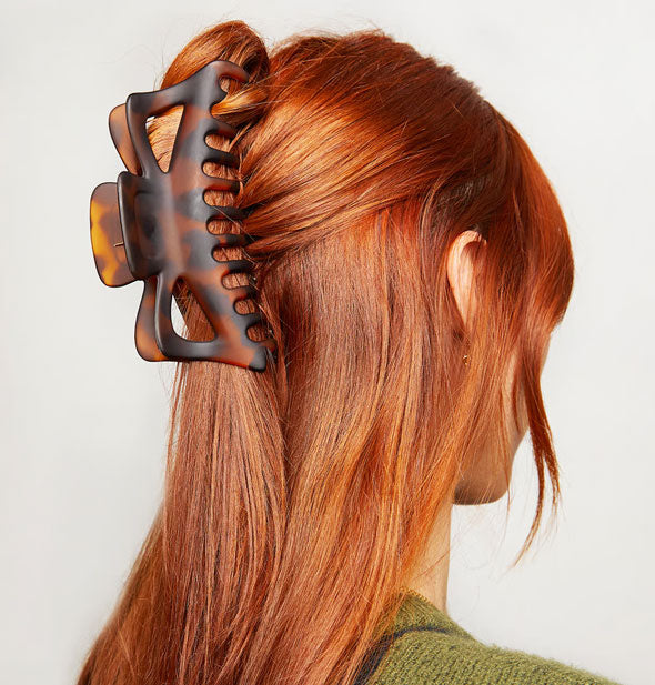 Model with straight red hair wears a jumbo-sized brown tortoise claw clip in a half-up twist hairstyle