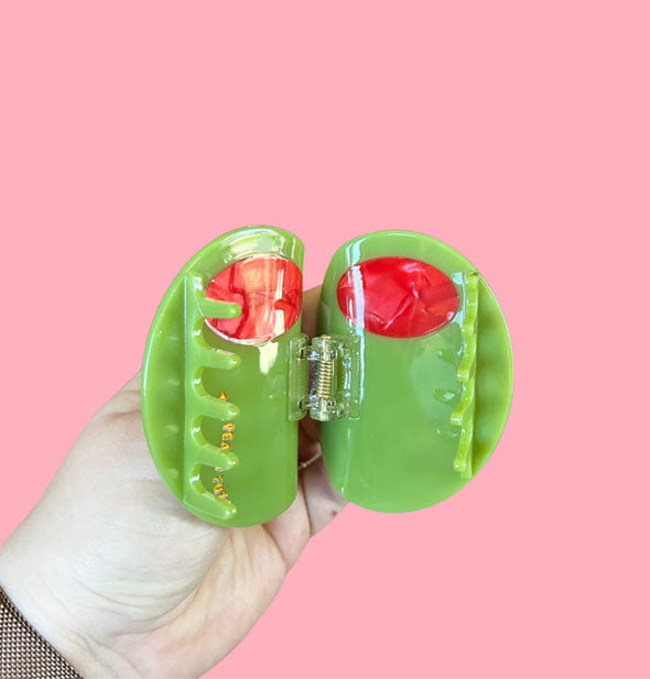 Model's hand holds an opened hair clip designed to resemble a large stuffed green olive