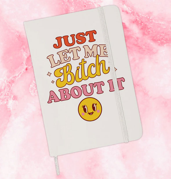 White journal on pink marble background says, "Just let me bitch about it" in red, pink, and yellow lettering of alternating styles above a yellow smiley face