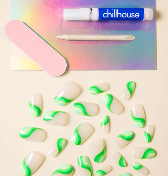 Contents of Chillhouse press-on nail kit: Nails with a wavy green design in an assortment of sizes, pink file, wooden cuticle pusher, and glue tube