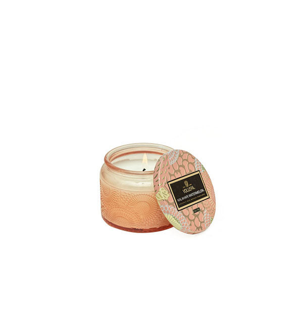 Peach-colored embossed glass jar candle with decorative metallic lid set to the side