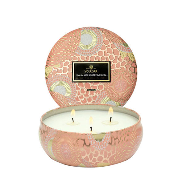 Peachy-pink decorative metallic Kalahari Watermelon Voluspa candle with lid removed to reveal three lit wicks