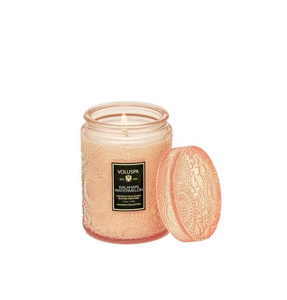 Peach-colored embossed glass Kalahari Watermelon Voluspa candle with matching lid set to the side