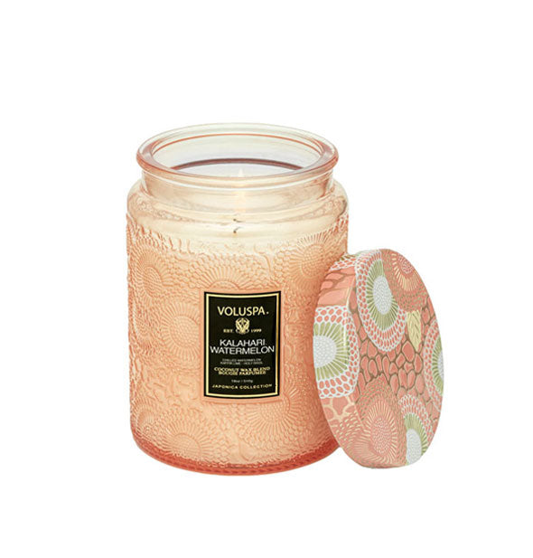 Peach-colored embossed glass Kalahari Watermelon Voluspa candle with matching metal lid set to the side