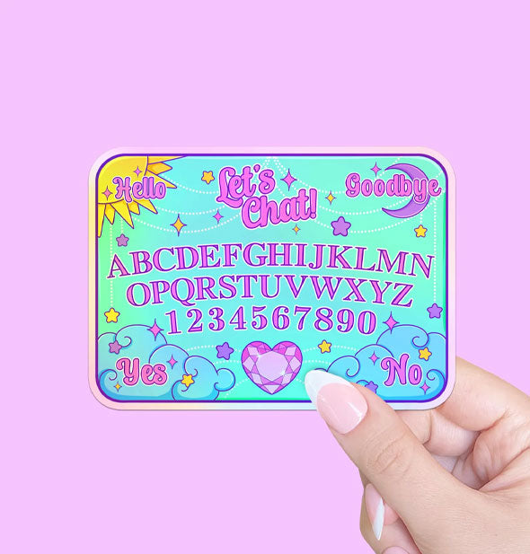 Model's hand holds a rectangular sticker designed as a Ouija board with a pastel kawaii aesthetic