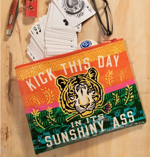 Kick This Day In Its Sunshiny Ass pouch appears to spill out playing cards, a pool ball, and other random personal items