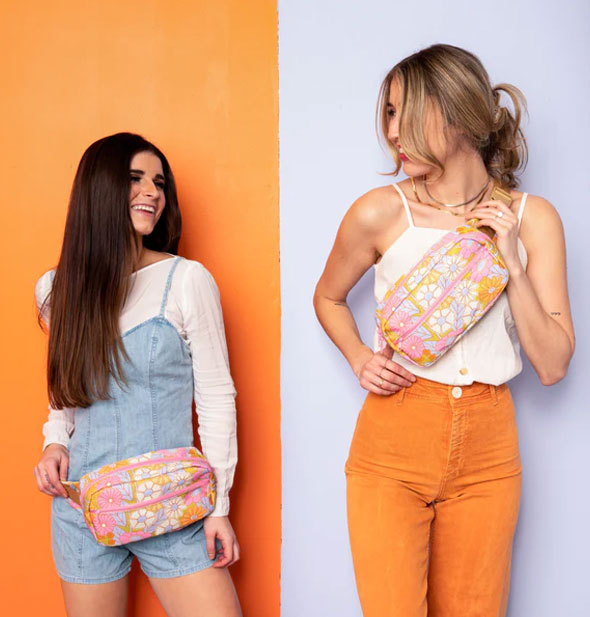 Models standing against an orange and blue backdrop each wear a Gatherin' Flower Hip Bag, one around hips and the other in a crossbody fashion