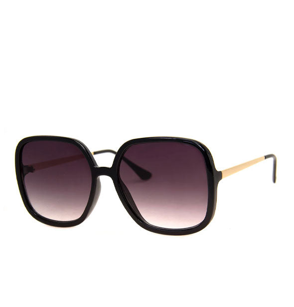 Pair of sunglasses with black front frame, gold temple arms, black temple tips, and dark purplish-gray lenses