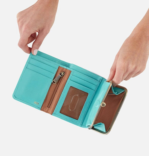 Model's hands hold open an aquamarine leather wallet to reveal interior pockets and brown details with gold hardware