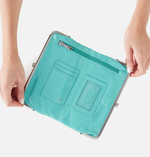 Model's hands hold open an aqua leather wallet to show pockets and slots inside