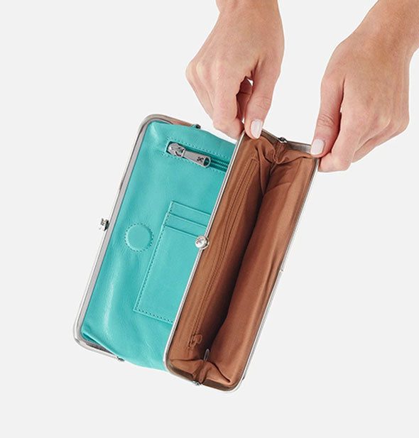 Model's hands hold open a section of an aqua leather wallet to show brown interior with additional zip pocket storage
