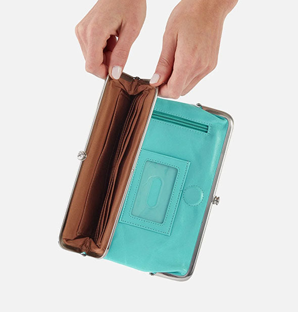 Model's hands hold open a pocket of an aqua leather wallet to show brown lining with slip pockets inside