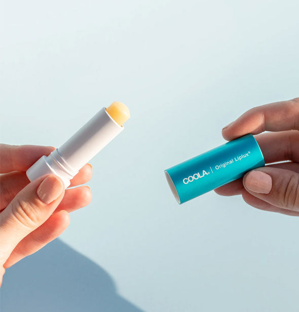 Model holds the blue cap and white tube of Coola Original Liplux sunscreen