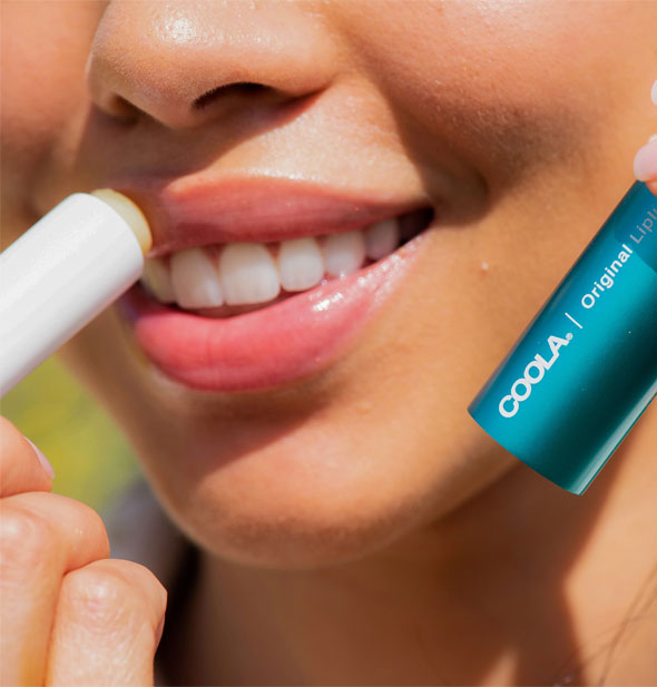 Smiling model applies Coola Original Liplux sunscreen to top lip