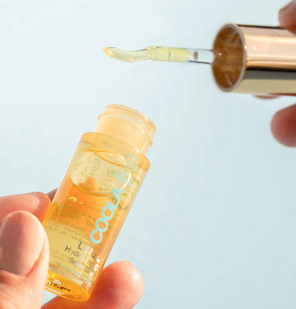 Model holds the applicator lid and bottle of a tube of Coola Liplux Hydrating Oil