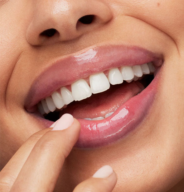 Smiling model touches fingertips to shiny, hydrated lower lip