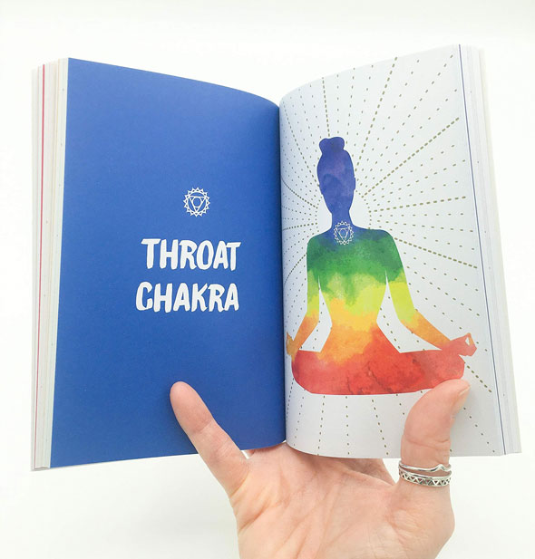 Model's hand holds open The Little Book of Chakras to a chapter titled, "Throat Chakra" opposite a colorful meditating figure
