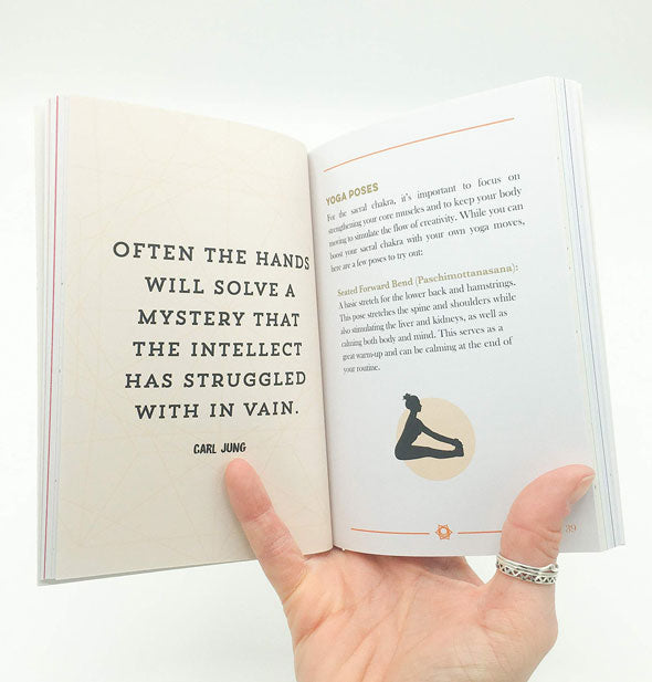 Model's hand holds open The Little Book of Chakras to a page featuring Carl Jung's words: "Often the hands will solve a mystery that the intellect has struggled with in vain."