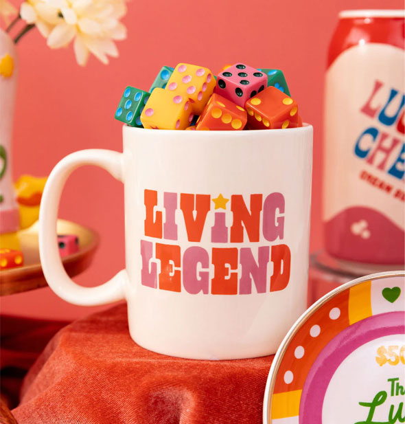 Living Legend coffee mug is staged on a red velvet surface and is filled with multicolored dice