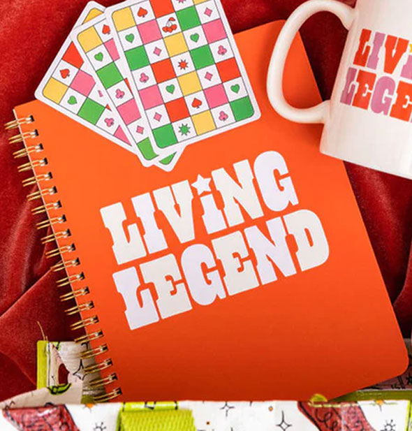 Living Legend notebook emerges from a bag and is flanked by checkered cards and a matching mug