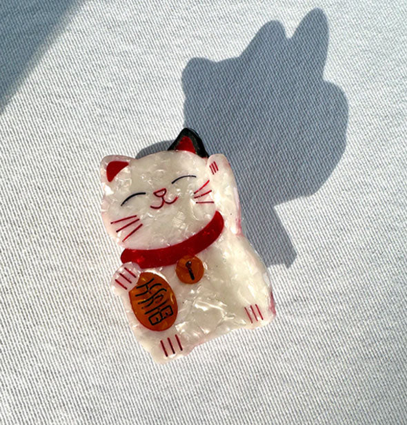 Red and white quartz-effect Japanese maneki-neko (lucky cat) hair clip rests on light wash denim