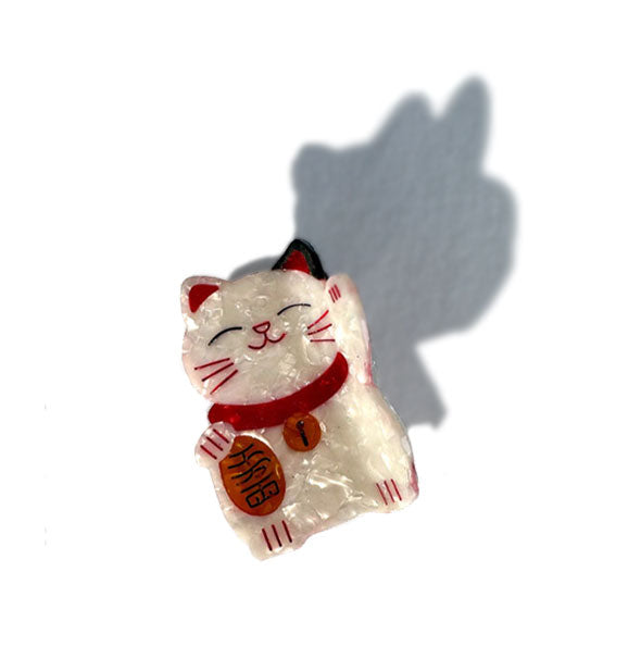 Red and white quartz-effect Japanese maneki-neko (lucky cat) hair clip rests on light wash denim