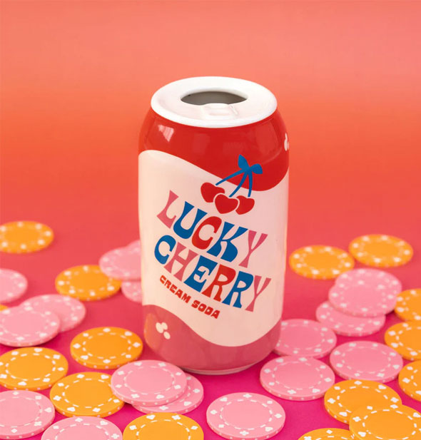 Ceramic flower vase shaped and painted to resemble a Lucky Cherry Cream Soda can rests on a reddish surface surrounded by pink and yellow poker chips