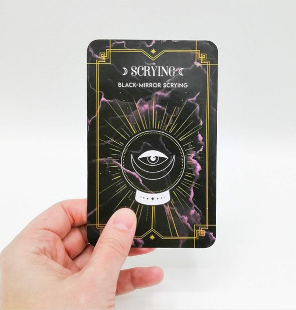 Model's hand holds a Black-Mirror Scrying card from the Magic Art of Fortune Telling oracle cards deck