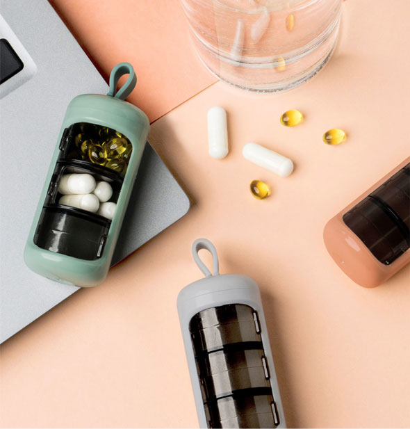 Green, orange, and gray Care Capsule pods lay on a surface with laptop, pills, and a glass of water