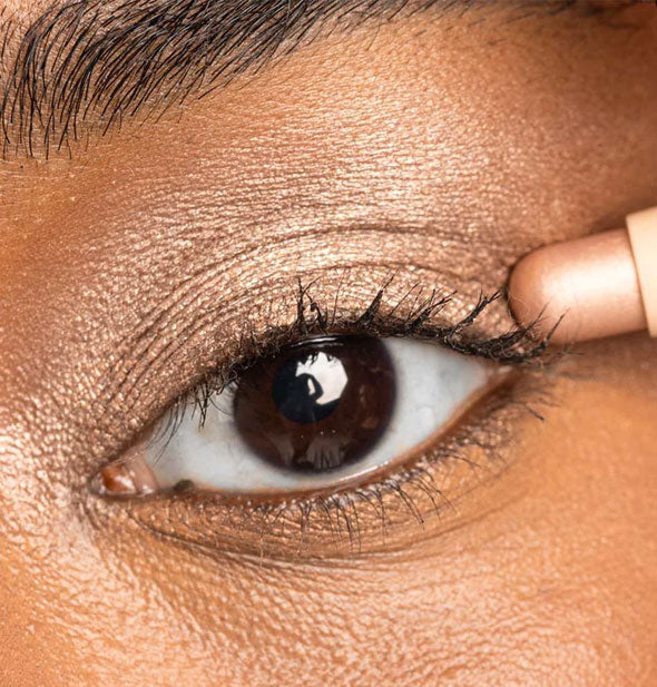 Model applies a champagne shimmer shade of stick eyeshadow to the outer corner of eyelid