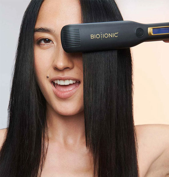 Model holds a section of smoothed, straight hair between the plates of a Bio Ionic styling iron in front of one eye