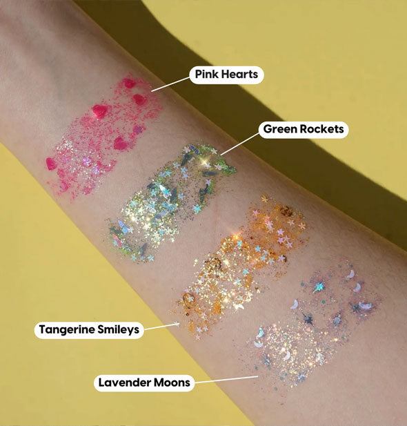 Model's arm wears applications of Pink Hearts, Green Rockets, Tangerine Smileys, and Lavender Moons body glitter shades