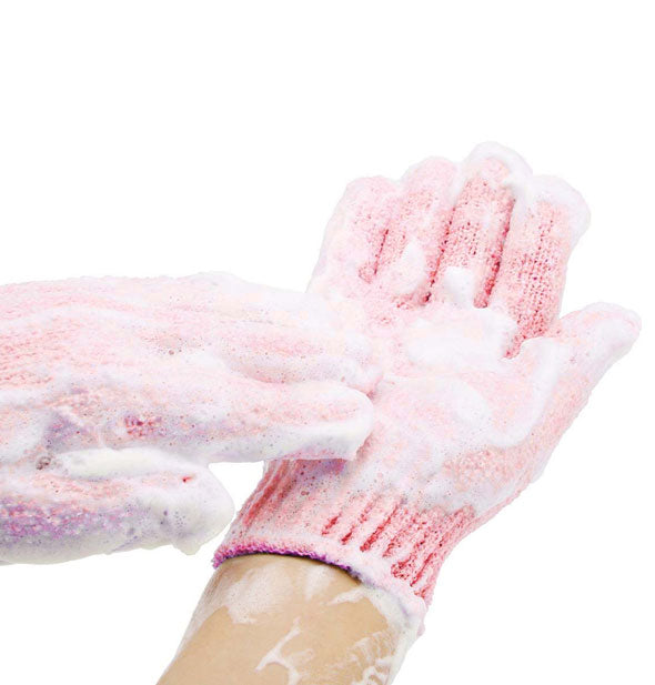 Model lathers cleanser into textured pink exfoliating bath gloves