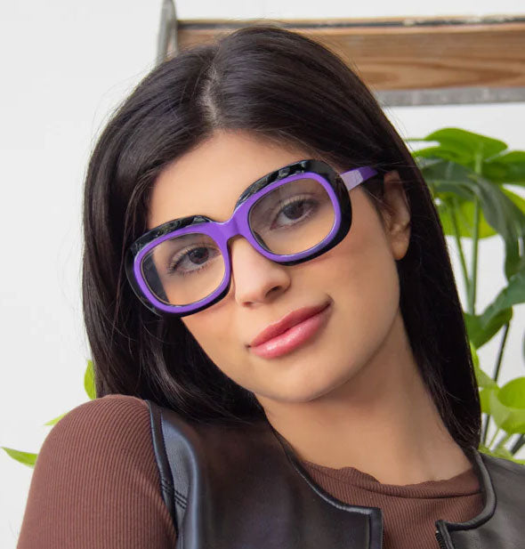 Model wears a pair of large rounded reading glasses with two-tone black and purple frame
