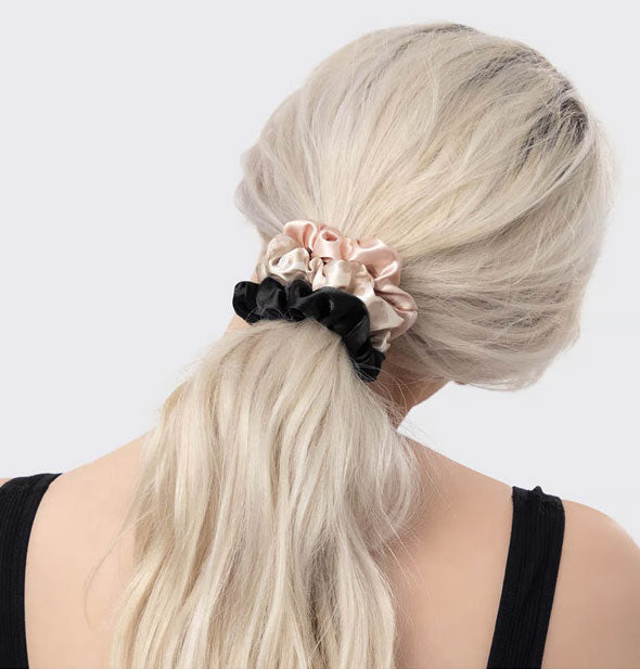 Model wears blush, beige, and black satin scrunchies in a low ponytail