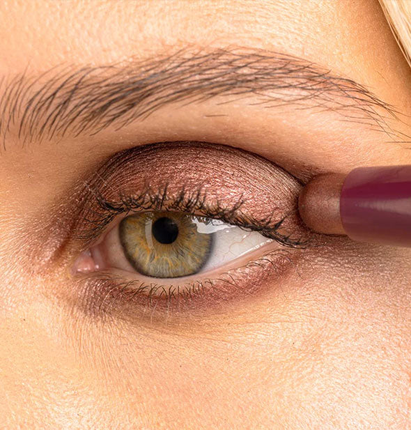 Model applies a shimmery rose shade of stick eyeshadow to the outer corner of eyelid