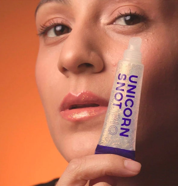 Model with sparkly lips holds a tube of Unicorn Snot out toward the camera