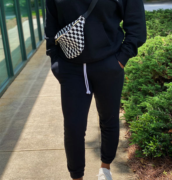 Model wears a black and white checkered sling bag worn in a crossbody style
