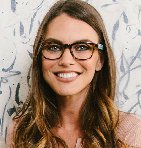 Smiling model wears a pair of brown tortoise and blue lattice reading glasses