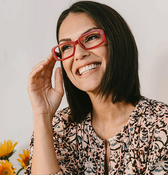 Smiling model wears a pair of rectangular red reading glasses