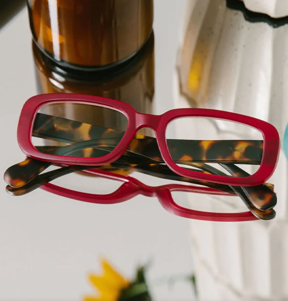 Red and brown tortoise rectangular reading glasses rest on a reflective surface