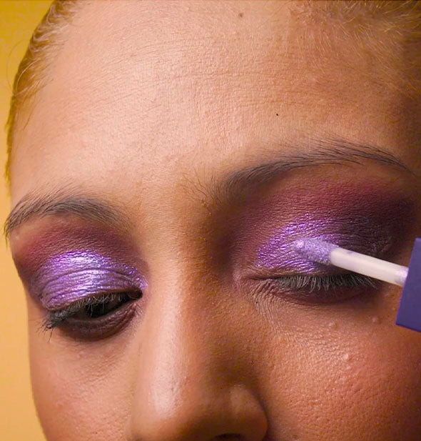 Model applies purple eyeshadow to lid with doe foot applicator