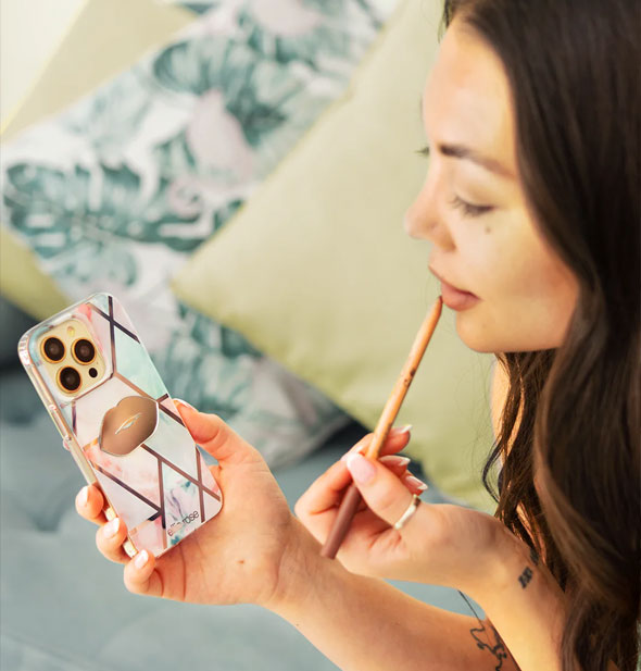 Model applies lip pencil using a lip-shaped mirrored phone decal attached to the back of her smartphone