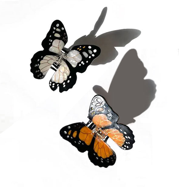 One white and one orange monarch butterfly claw clip, each with spotted black wing edging and gold line details
