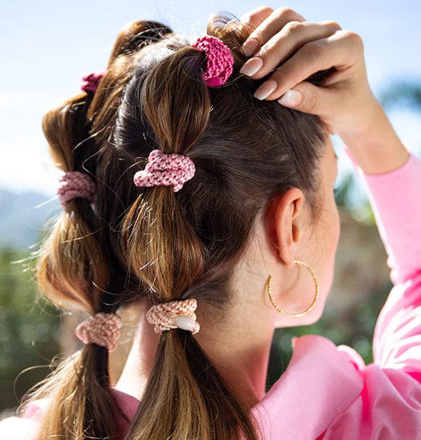 Model wears pigtails secured with woven hair ties in an assortment of pink shades