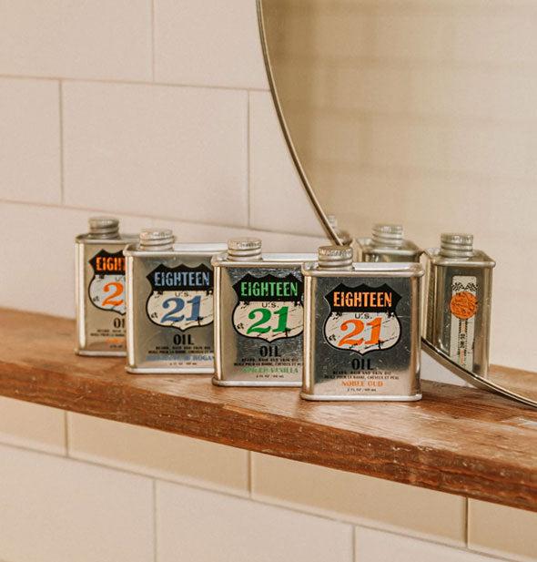 Grouping of Eighteen 21 Oil cans on a wooden shelf against a white tiled background with round mirror