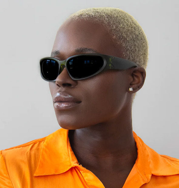 Model in bright orange top wears black wraparound sunglasses with dark lenses