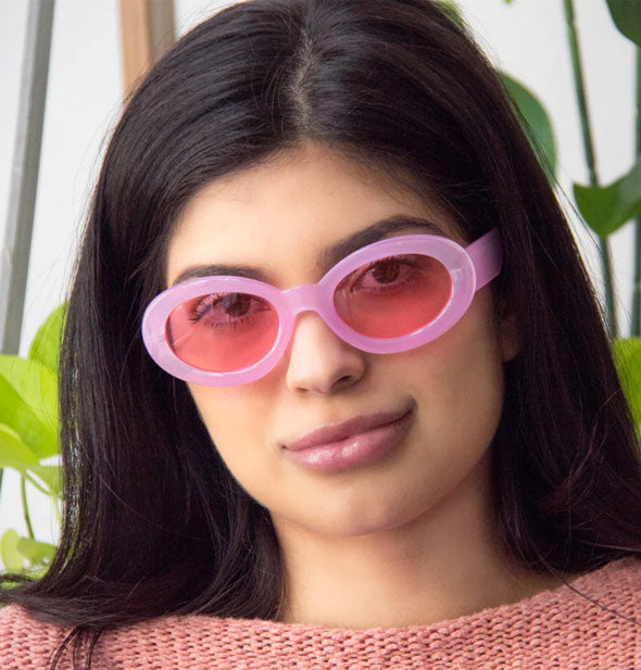 Model wears a pair of rounded pink sunglasses with rosy lenses
